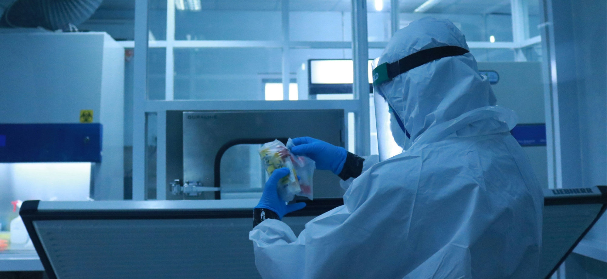 Person in a lab coat and protective gear working with equipment in a laboratory setting.
